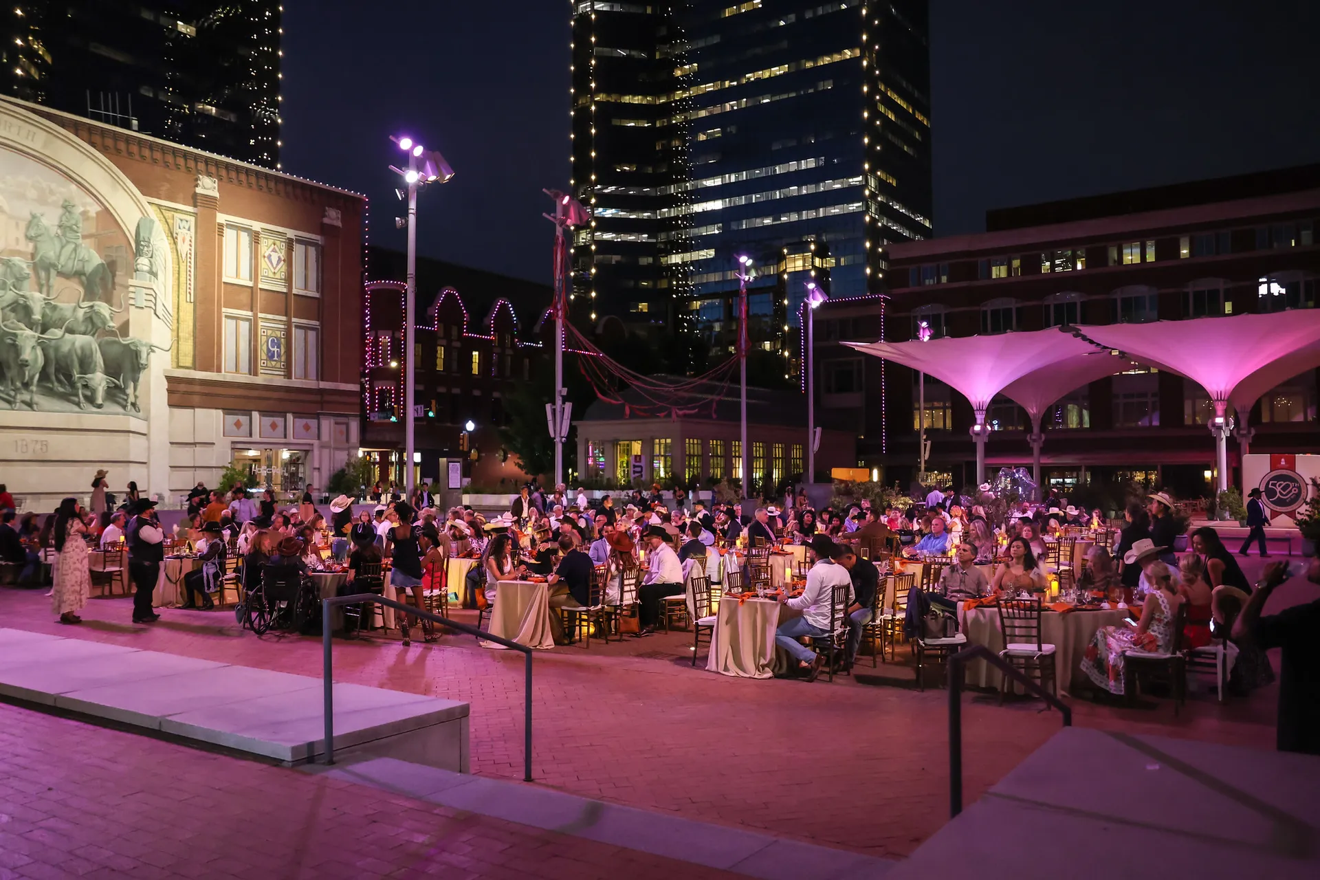 Many full dinner tables on a patio dimly lit by streetlights