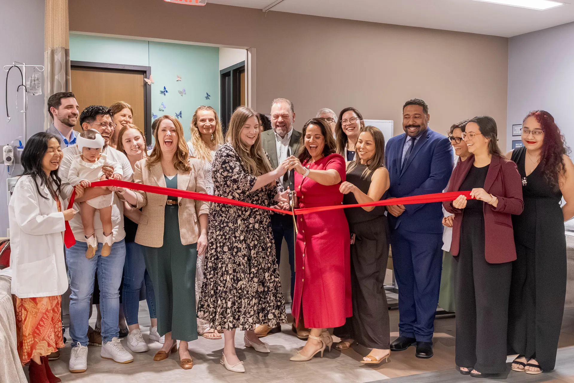A group of people gathered in front of a ribbon, with two people cutting it with oversized scissors