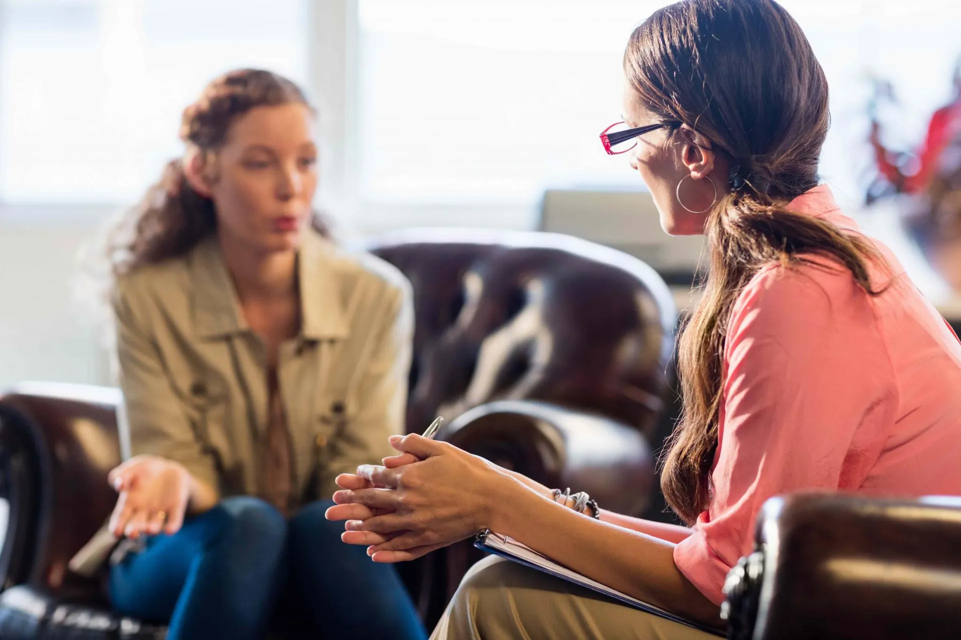 A woman sits in a brown seat and leans forward as she talks to her counselor who is listening intently 