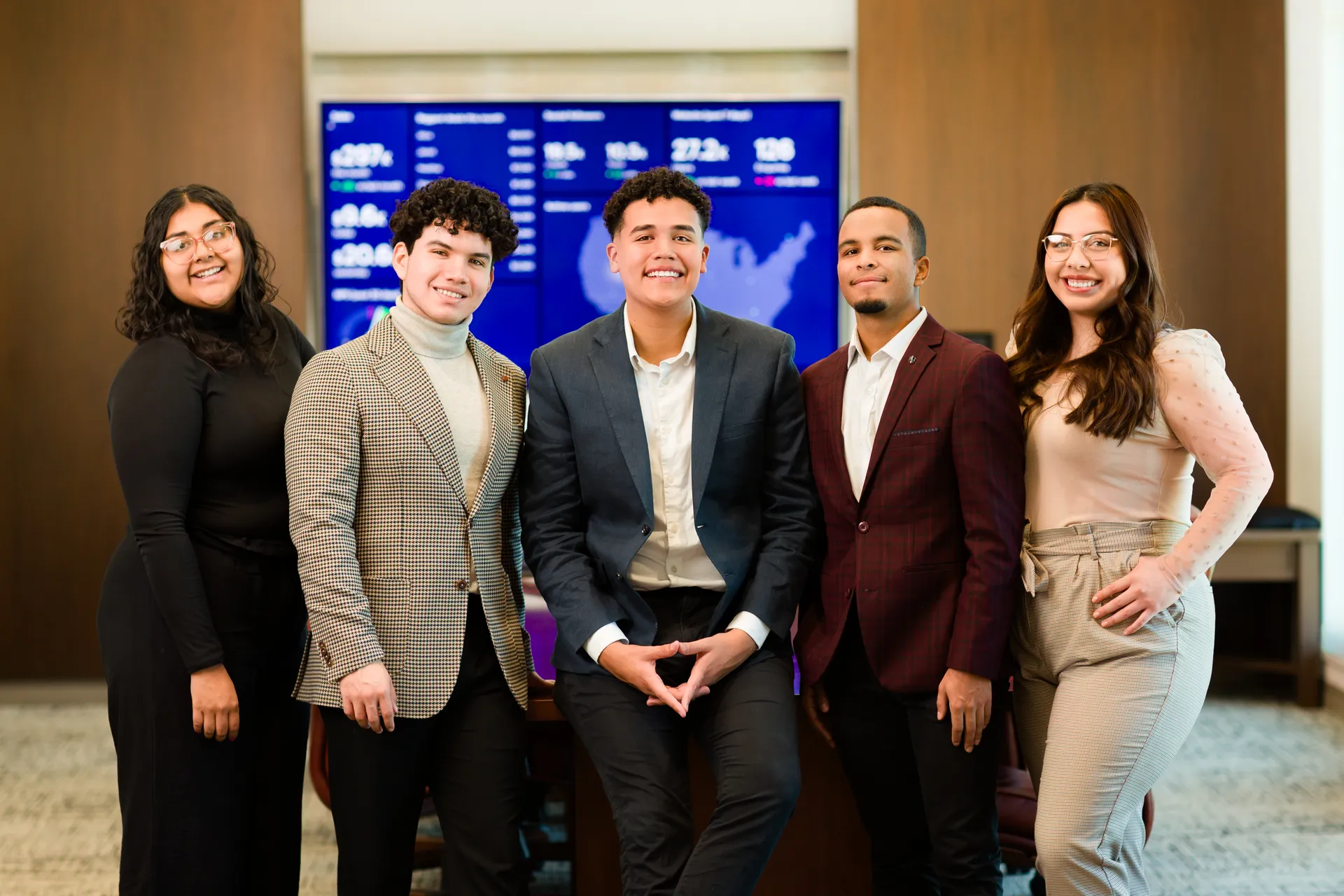Five students in formal wear standing in front of TV with map displayed