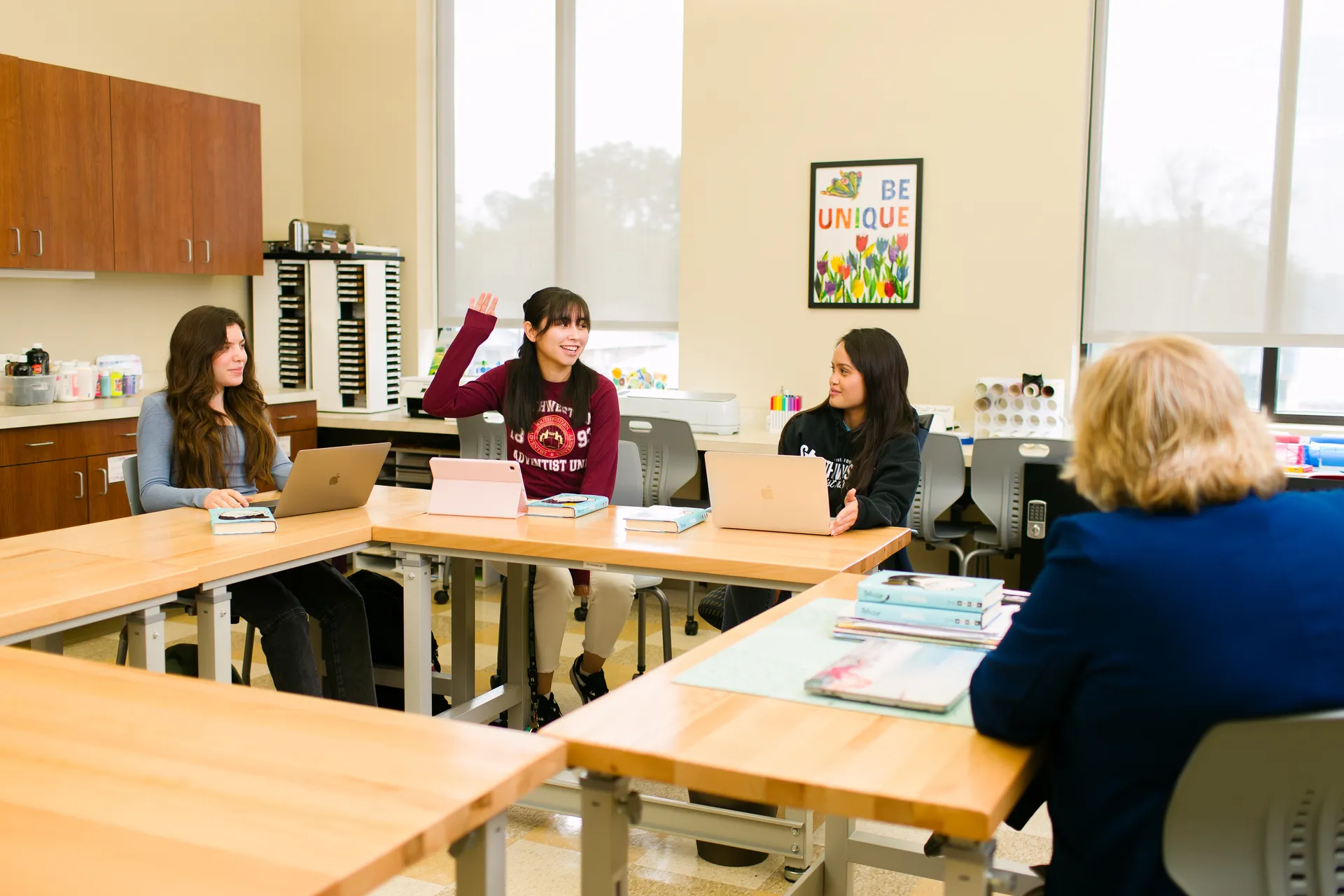 Three students sitting around a box of tables discussing while a teacher watches