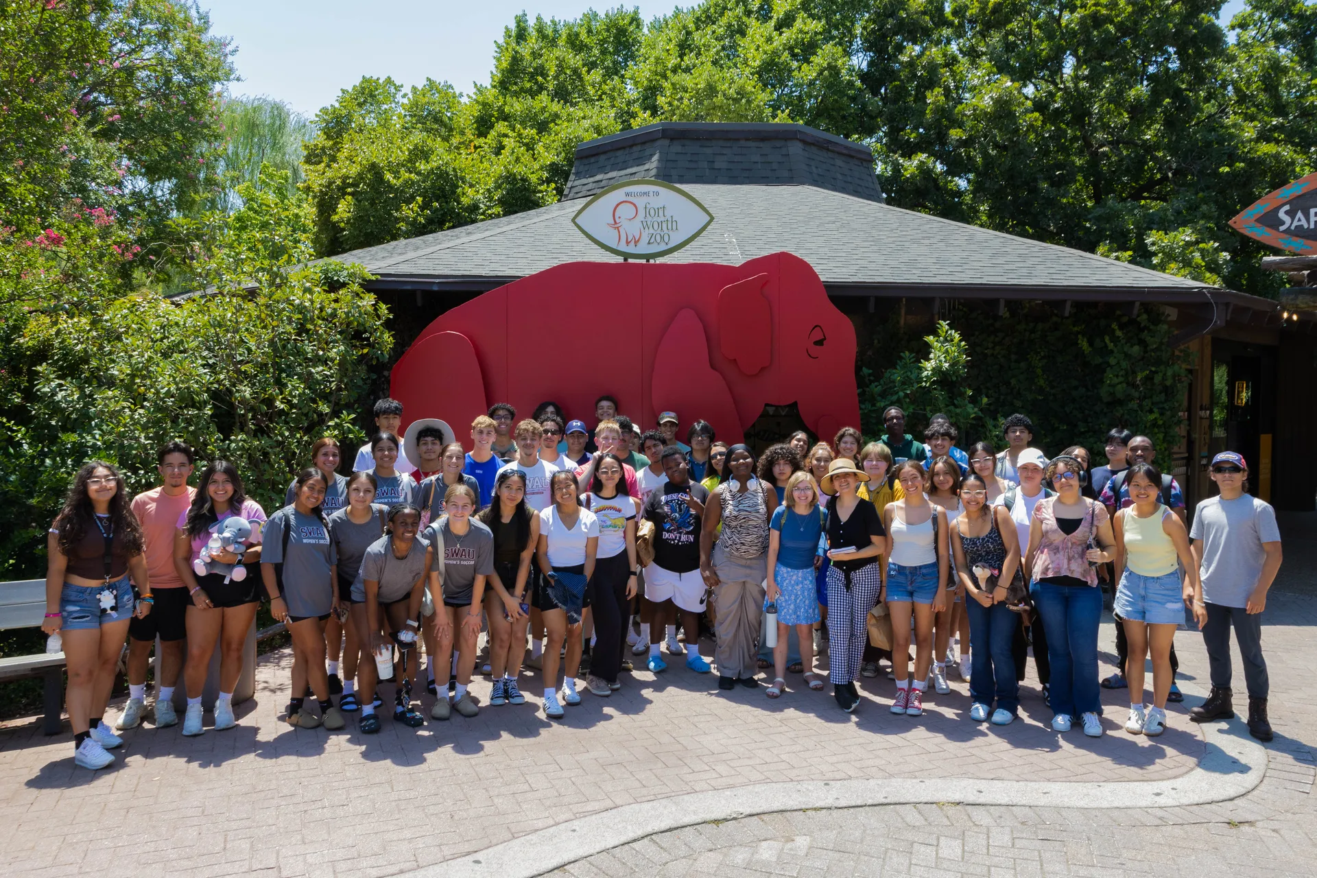 group photo of students standing in front of fort worth zoo elephant sign