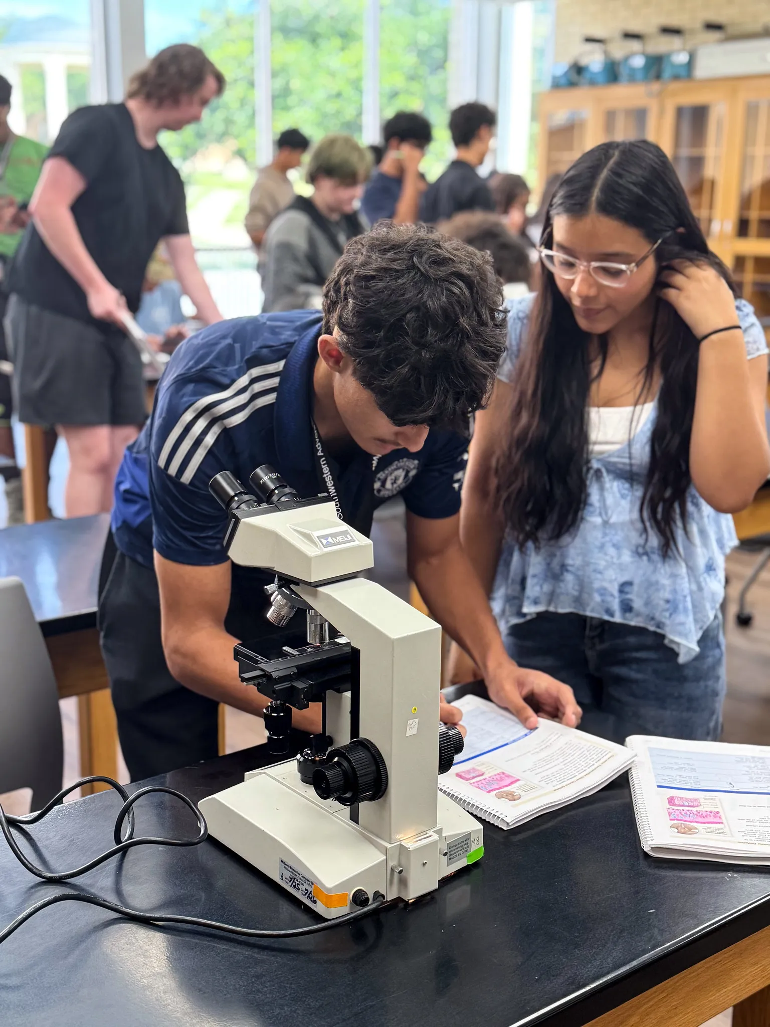 student writing in a notebook next to a microscope