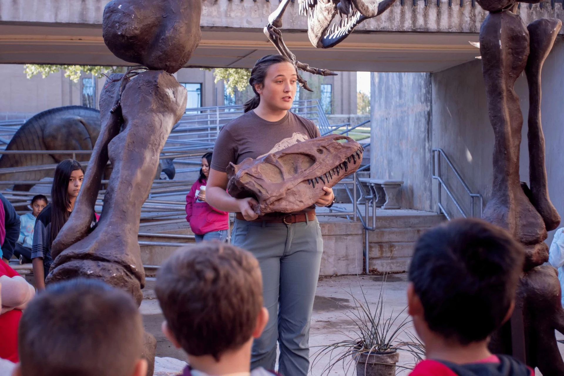 A dinosaur museum worker talks to the audience of children as she explains the dinosaur skull in her hands