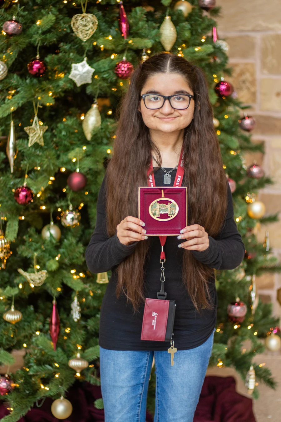 Caroline Torres poses in front of a Christmas tree holding a box containing the Mizpah ornament