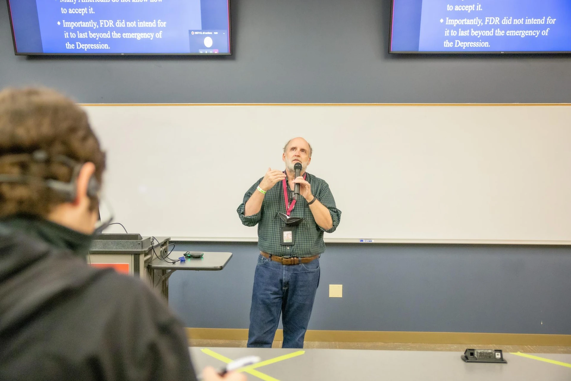 Dr. Jones standing in front of a classroom teaching students as he holds a microphone.