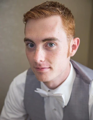 A young man with short, naturally red hair looks up and gently smiles