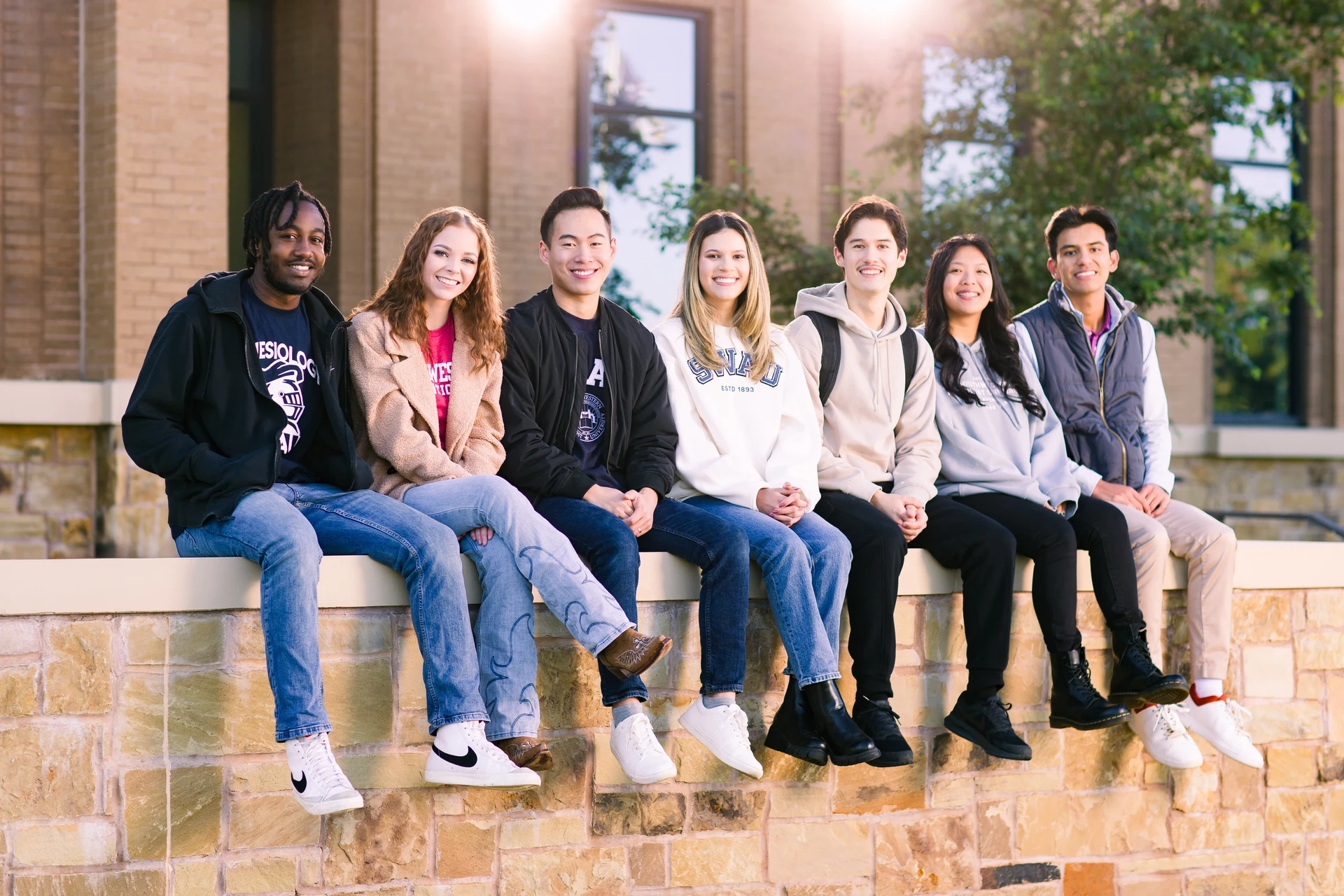 Diverse group of Adventist university students in Texas sitting on a wall smiling at the camera