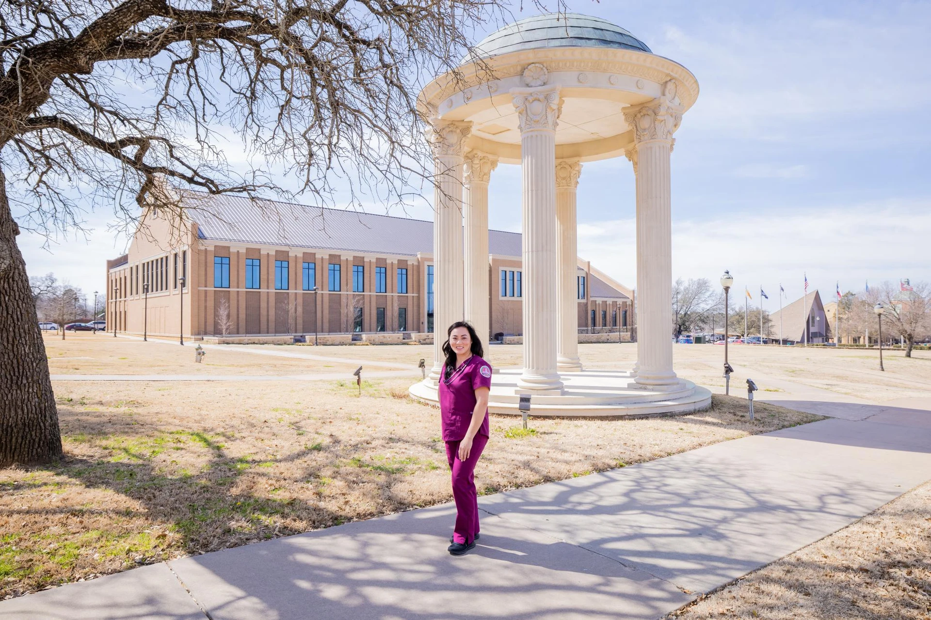 Linh Vu poses in SWAU scrubs in front of the rotunda with the nursing building in the background