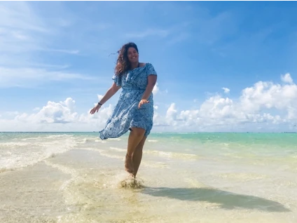 Walking on a beach, a young woman wears a blue dress that blows in the wind
